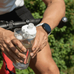 Manos de deportista sosteniendo un bidón transparente marcado en mililitros para registrar el volumen de líquido ingerido.
